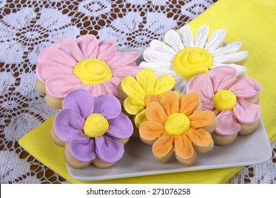 Fancy Home Made Spring Flowers Sugar Cookies With Royal Icing Petals Piped On. Served On A Square Plate With Yellow Napkin Underneath. 