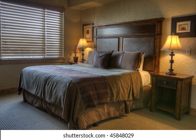 Fancy Hotel Room Highlighted By A Shutters Covered Window And Two Night Table Lamps.