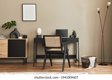 Fancy interior design of home office space with stylish chair, desk, commode, black mock up poster frame, lapatop, book, desk organizer and elegant presonal accessories in home decor. Template. 