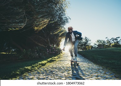 A Fancy Mature Bearded Black Guy In A Fashionable Costume With A Hat And A Necktie, With A Golf Club In His Hand And A Cigar In His Mouth, Is Rolling On A Skateboard On Paving-stone On The Sunset