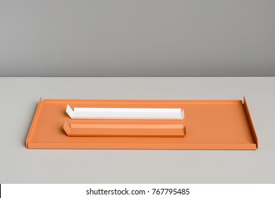 Fancy metallic orange support with two small orange and white pedestals on the light gray surface on the dark gray wall background indoors. Closeup horizontal photo.