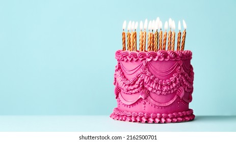 Fancy pink birthday cake with vintage style buttercream frills and ruffles and gold birthday candles against a blue background - Shutterstock ID 2162500701