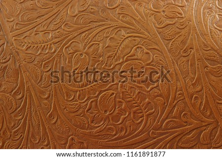 A fancy tan brown light colored background made of imprinted leather, with flowers and floral and cowboy western designs.