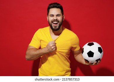 Fancy Young Bearded Man Football Fan Pull Tear Yellow T-shirt Cheer Up Support Favorite Team Hold Soccer Ball Isolated On Plain Dark Red Background Studio Portrait. People Emotions Lifestyle Concept