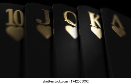 A fanned out royal flush suit of five black casino playing cards with gold markings on a dark classy background - 3D render - Shutterstock ID 1942553002