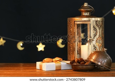 Fanoos, dates and gift box on wooden table against black background. Ramadan celebration