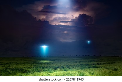 Fantastic Dramatic Image: UFO Or Alien Spacecraft  Inspect Green Grass Field With Bright Spotlight In Dark Stormy Night Sky. 