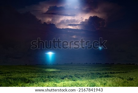 Fantastic dramatic image: UFO or alien spacecraft  inspect green grass field with bright spotlight in dark stormy night sky. 