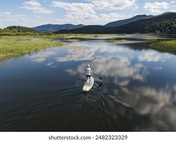 Fantastic mountain lake scenery and a stand up paddleboarder paddling on calm water with beautiful sky reflection, aerial shot. - Powered by Shutterstock