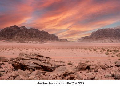 Fantastic view of the endless arid valley, Wadi Rum desert, Jordania. Spectacular sky with large red dramatic clouds, mountain range, lots of red sand and a few bushes and rocks in the background.
