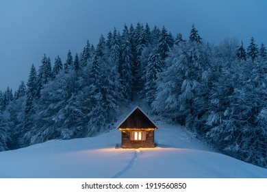 Fantastic Winter Landscape With Glowing Wooden Cabin In Snowy Forest. Cozy House In Carpathian Mountains. Christmas Holiday Concept