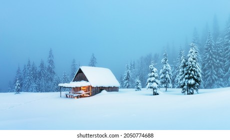 Fantastic Winter Landscape With Glowing Wooden Cabin In Snowy Forest. Cozy House In Carpathian Mountains. Christmas Holiday Concept