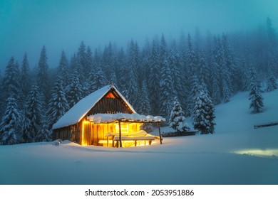 Fantastic Winter Landscape With Glowing Wooden Cabin In Snowy Forest. Cozy House In Carpathian Mountains. Christmas Holiday Concept