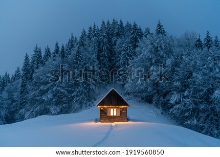 Fantastic winter landscape with glowing wooden cabin in snowy forest. Cozy house in Carpathian mountains. Christmas holiday concept