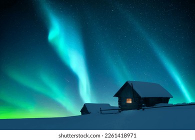 Fantastic winter landscape with wooden house with light in window in snowy mountains and northen light in night sky. Christmas holiday and winter vacations concept - Powered by Shutterstock