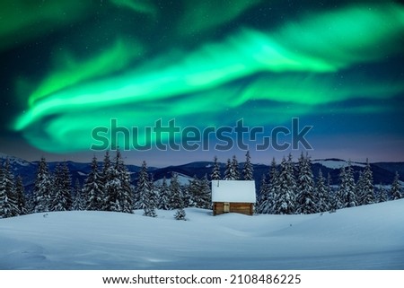 Fantastic winter landscape with wooden house in snowy mountains and northen light in night sky. Christmas holiday and winter vacations concept