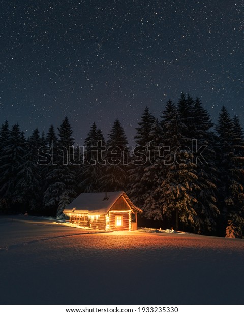 Fantastic winter landscape with wooden\
house in snowy mountains. Starry sky with Milky Way and snow\
covered hut. Christmas holiday and winter vacations\
concept