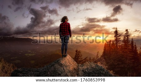 Fantasy Adventure Composite with a Girl on top of a Rock Cliff with Beautiful Nature Landscape in Background during Sunset or Sunrise. Concept: Hike, Freedom, Explore, Journey