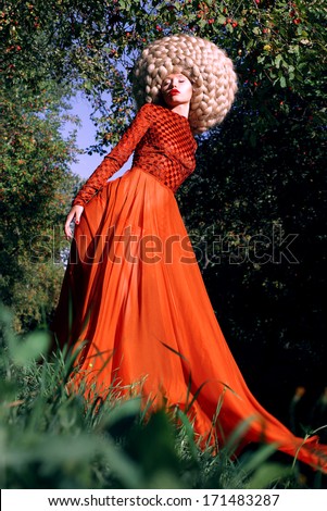 Fantasy. Artistic Stylized Woman in Trendy Red Dress and Big Frizzy Wig