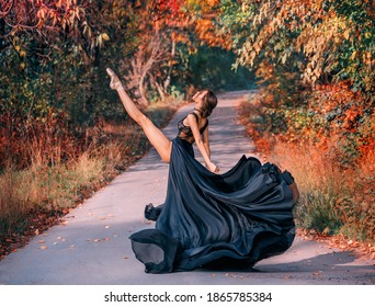 Fantasy Beautiful girl ballerina dancing on road. Autumn nature background trees. Fashion model posing in motion. Long silk black dress, skirt flies in wind. Woman ballet dancer leg is raised in split - Powered by Shutterstock