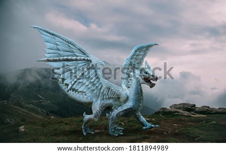 Fantasy dragon stands on the top of the mountain. A huge dangerous animal with large, sharp wings. Beautiful alpine nature background, dramatic gray blue sky with white clouds.