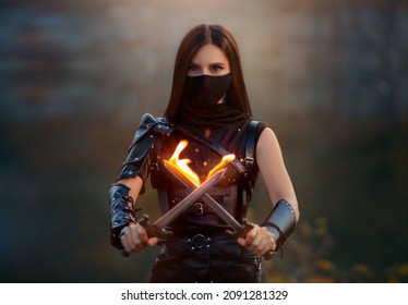 Fantasy fighting woman assassin holds in hands burning daggers. Red-haired girl warrior in black leather costume. ninja soldier with knives, fire magic. Strong face hidden behind mask, blue eyes