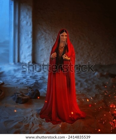 Fantasy girl Mystery arabic woman in red long dress stands in desert long silk abaya dress. clothes gold Golden Mask chain Burka hide face Oriental fashion Eastern style. Sand dunes night room fire.