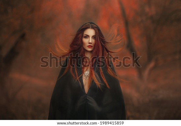 fantasy gothic woman dark witch. Red-haired evil\
Girl demon in black dress cape hood. Long hair flutters fly in\
wind. Dark dense deep autumn forest orange colors trees. Medieval\
dress, silk clothes.
