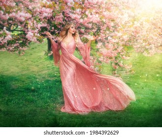 Fantasy happy girl elf princess walks in spring blooming garden. Pink flowers sakura tree green grass summer nature. long lace dress wide sleeves flies in wind motion. Blonde woman queen. vintage gown
