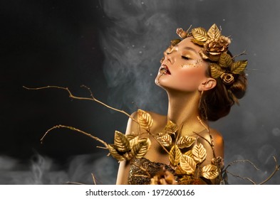 Fantasy portrait of woman, golden skin body. Girl goddess in wreath gold roses dress. Beautiful face steel glitter art makeup. Art photo black background white blue smoke. Girl princess Fashion model 