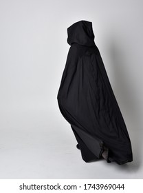 fantasy portrait of a woman with red hair wearing dark leather assassin costume with long black cloak. Full length standing pose with back to the camera  isolated against a studio background.
