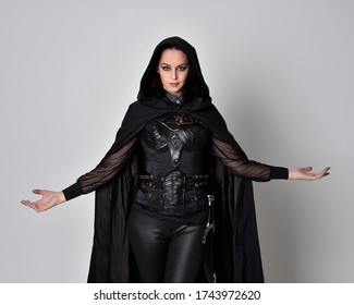 fantasy portrait of a woman with red hair wearing dark leather assassin costume with long black cloak. close up, 3/4 pose  isolated against a studio background.