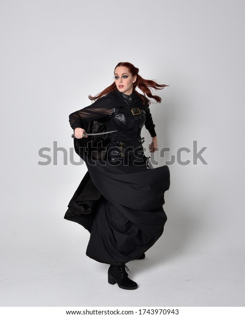 fantasy\
portrait of a woman with red hair wearing dark leather assassin\
costume with long black cloak. Full length standing pose holding a\
weapon,  isolated against a studio\
background.