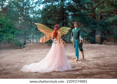 fantasy romantic couple in love. Prince happy man goes to meet girl princess in forest. Elf woman in pink dress, train back rear view. Fairy wings costume pixie goddess. Long red hair art silver tiara