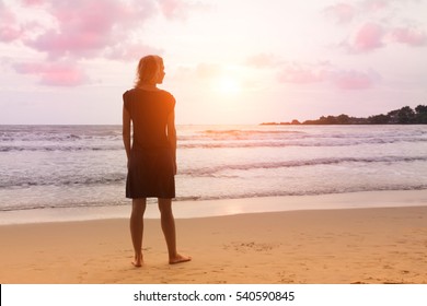 Fantasy scene: young girl is standing at sunset sea beach and dreaming or thinking about something. Woman is looking to horizon.