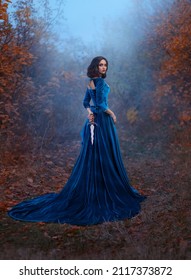 Fantasy warlike medieval woman queen holds metal vintage dagger blade weapon in hands hides behind back. Background forest fog night. Blue velvet luxurious royal dress. Girl princess warrior rear view