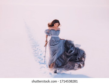 Fantasy Warrior Princess Redhead Hair Elf Walking Winter Frost White Snow Nature. Young Beauty Woman Runs. Queen Holds Hands Magic Blade Sword. Blue Silk Long Vintage Dress Fluttering Fly Wind Motion 