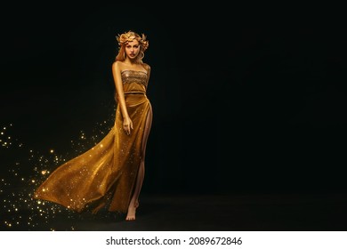 Fantasy woman, face in gold paint. Golden shiny skin. Fashion model girl, image goddess. Glamorous crown, wreath roses, jewellery accessories. metallic makeup. Gold fabric evening long dress waving