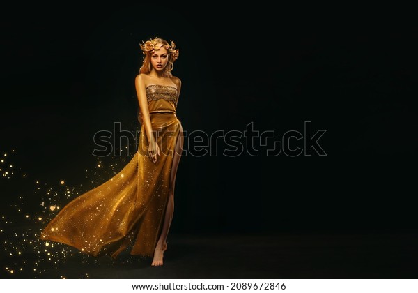 Fantasy woman, face in gold paint. Golden shiny
skin. Fashion model girl, image goddess. Glamorous crown, wreath
roses, jewellery accessories. metallic makeup. Gold fabric evening
long dress waving