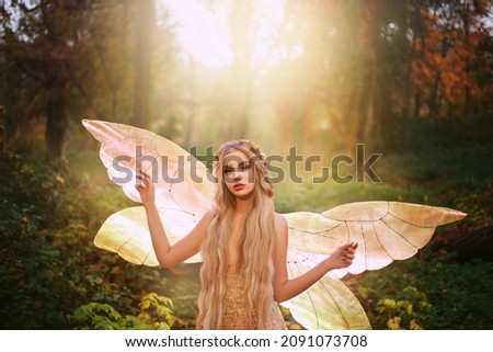 Fantasy woman fairy fashion model in fabolous summer forest. Girl elf goddess of nature. Golden pixie wings costume, shiny glow dress. Cute face lady princess gold queen of butterfly, sun magic light