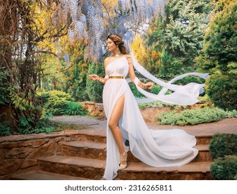 Fantasy woman greek goddess walks in spring garden purple flowers green tree nature day sun light. Sexy girl queen antique style white silk dress fly, gold diadem on red hair, lady going down stairs.