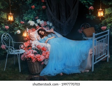 Fantasy Woman Sleeping Beauty Lies Sleep On Comfortable Bed, Mattress, Soft Pillow. Background Mystical Garden, Night, Peonies Flowers Green Trees. Fairy-tale Girl Princess In Blue Dress. Sweet Dreams