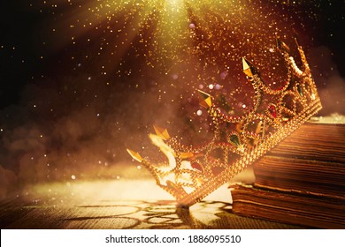 Fantasy world. Beautiful golden crown and old books lit by magic light on table - Shutterstock ID 1886095510