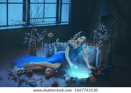 Fantasy young beautiful sorceress woman. long blue dress touch divine old mirror. Predictor future fairy tale Snow White. magic power wind light spell. Mystic gothic art photo dark black medieval room