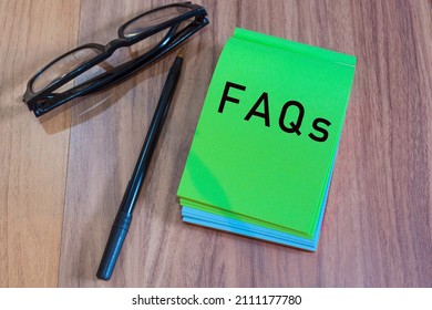 FAQs Text On Green Notepad With Glasses And Pen On A Desk. Top View