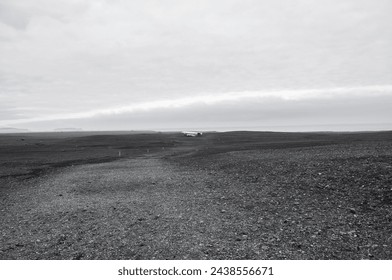 Far away an abandoned crashed United States Navy DC plane wreckage lies on a flat black sand ground in a coastline of Southern Iceland - Powered by Shutterstock