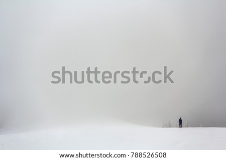 Far away lonely figure of a man standing outdoors in winter