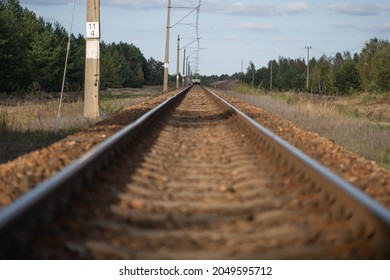 Far Away On The Horizon, The Locomotive Of The Train Is Moving Towards The Camera Along The Railway Rails On A Clear Summer Day