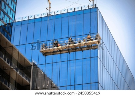 Far and corner shot of three window washers on a hanging scaffold on a commercial building with blue glass