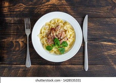 Farfale pasta or bows of bacon, pepper and basil under white creamy sauce in a white plate on a dark wooden background. Top view. Menu. - Powered by Shutterstock